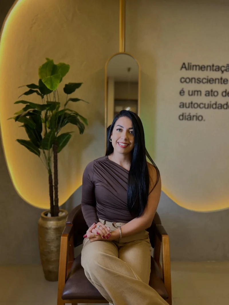Izabela sentada no consultório, diante do nicho iluminado e da frase na parede